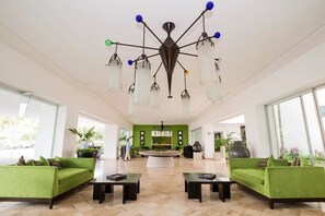 A spacious lobby with a green sofa, a coffee table, and a unique ceiling light fixture. - One Bedroom Suite at Sea Garden (Las Jarretaderas)