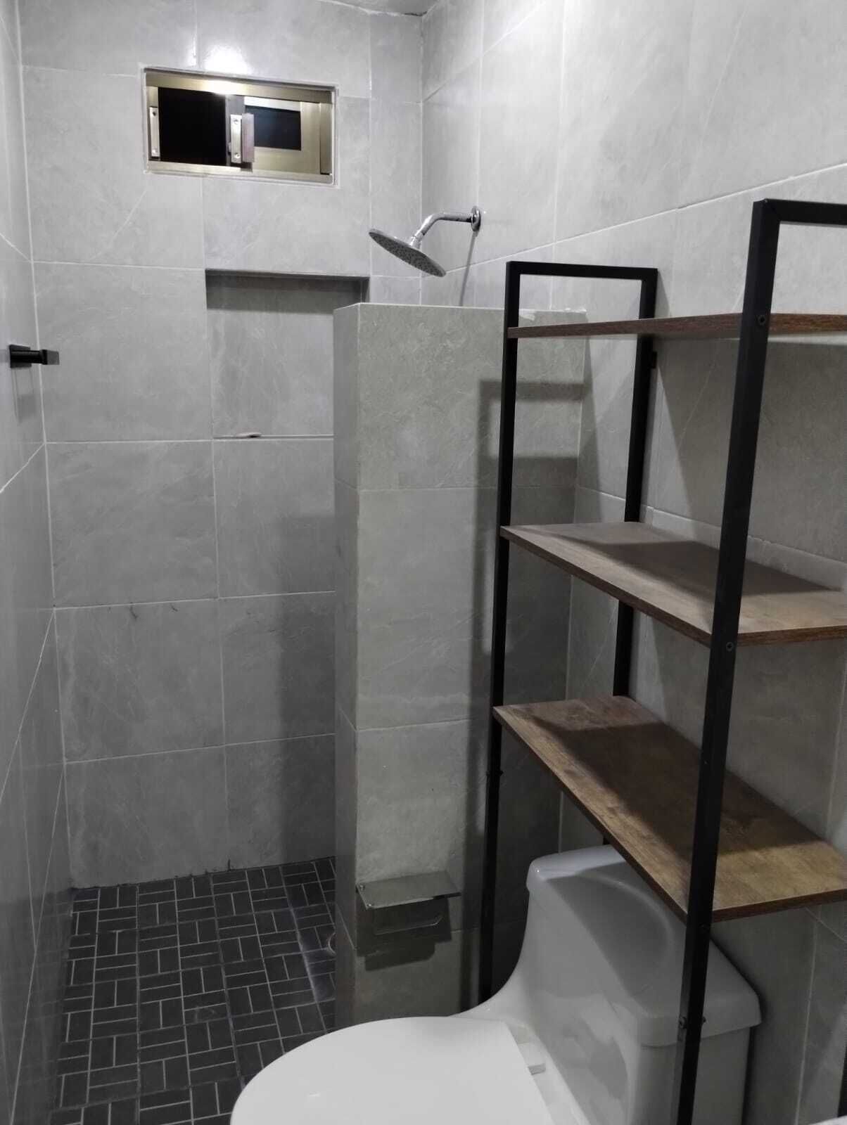 A bathroom with a shower, a toilet, and a shelf unit.