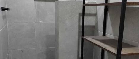 A bathroom with a shower, a toilet, and a shelf unit.