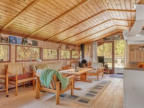 Ein Interieur einer Holzhütte mit Holzbalkendecke, einem Essbereich, einer Couch und einem Kamin.