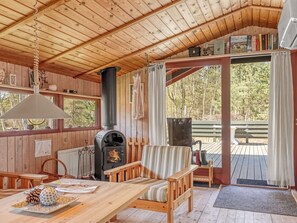 Ein gemütliches Blockhaus-Interieur mit Holzbalkendecke, Kamin, Esstisch, einer Couch und Blick ins Freie.
