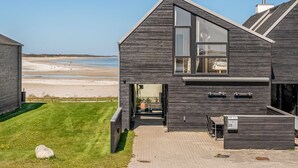 A modern house with a large window, a paved driveway, and a view of the beach.