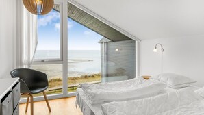 A bedroom with a large window, a bed, a desk, and a chair.