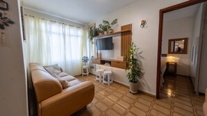Un salon avec un canapé, un téléviseur, une petite table et une plante en pot.