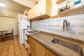 A kitchen with a granite countertop, stainless steel sink, white cabinets, and patterned backsplash tiles. - Apartamento com Garagem a 450m da Praia do Forte (Praia Grande)