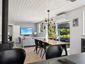 Ein modernes Wohnzimmer mit großem Fernseher, einem Essbereich mit Holztisch und -stühlen sowie einem Kamin.