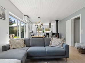Ein modernes Wohnzimmer mit einer grauen Couch, einem Essbereich mit Holztisch und einer Küche mit schwarzem Herd.
