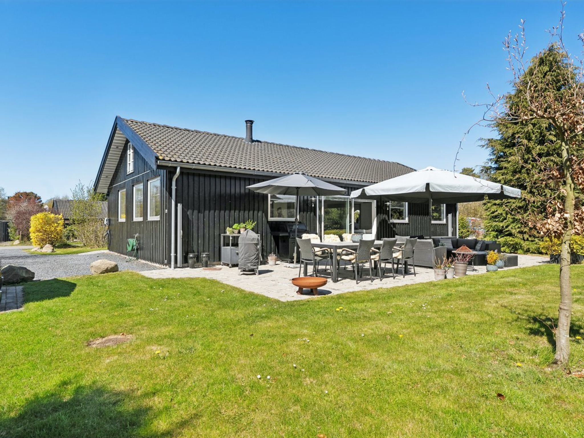 Ein modernes Haus mit Terrasse, Gartenmöbeln und einem großen Baum.