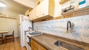 Una cocina con encimera de granito, pileta de acero inoxidable, muebles de color blanco y azulejos decorativos en la pared.