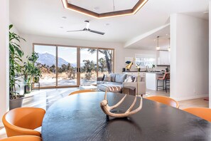 A modern living room with a dining table, orange chairs, and a large window with a mountain view. - High West House Retreat - 3 Residences (Carbondale)