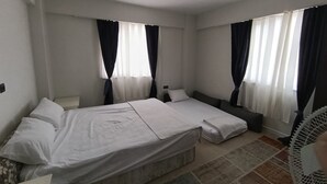 A hotel room with a large bed, two bedside tables, a small sofa, and a standing fan.