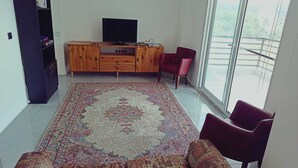 A living room with a large rug, a sofa, a TV, a cabinet, and a chair.