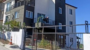 A multi-story residential building with balconies, a gated entrance, and a clear sky.