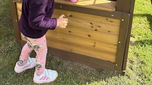 Ett barn leker med leksaker i ett litet trähus med fönster och en hylla.