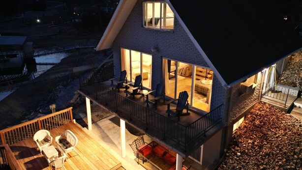 Een tweelaags huis met een balkon, buitenmeubels en een groot raam.