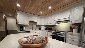 Een moderne keuken met witte kastjes, een houten kom op het aanrecht en roestvrijstalen apparatuur.