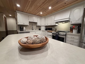 Een moderne keuken met witte kastjes, een houten kom op het aanrecht en roestvrijstalen apparatuur.