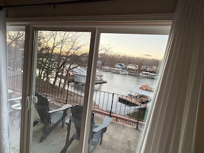 A balcony with chairs and a table, overlooking a river with boats and houses. - Secluded A-Frame Lakefront with Sun Deck and Sauna (Lake Ozark)