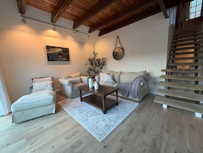 Una sala de estar con sofá, sillón, mesa de centro y una escalera.