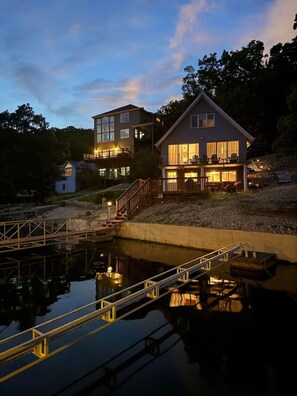 Een pand aan het water met een steiger, een groot huis met meerdere verdiepingen en een kleiner bijgebouw ernaast.