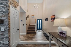 A hallway with a stone wall, a blue door, a staircase, and a lamp on a table. - Epic Escape with Hot Tub close to Canyons! (Cottonwood Heights)