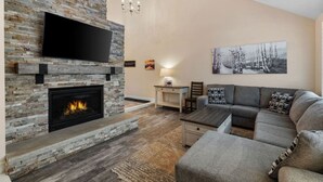 Una sala de estar con chimenea de piedra, un televisor de pantalla plana montado encima, un sofá gris, una mesita y un cuadro en la pared.