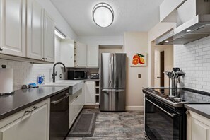 Cocina moderna con armarios blancos, electrodomésticos de acero inoxidable y encimera negra.