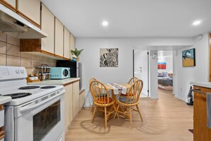 Une cuisine compacte équipée d’une cuisinière, d’un four à micro-ondes et de placards, qui donne sur un coin repas avec une table et des chaises.