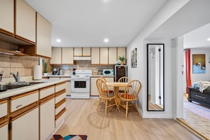 A modern kitchen with wooden cabinets, a dining table with chairs, a microwave, and an oven.