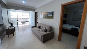 Una sala de estar con sofá, mesa de comedor con sillas, televisor y un cuadro en la pared.