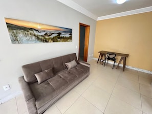 Een woonkamer met een bruine bank, een eettafel met stoelen en een schilderij aan de muur.