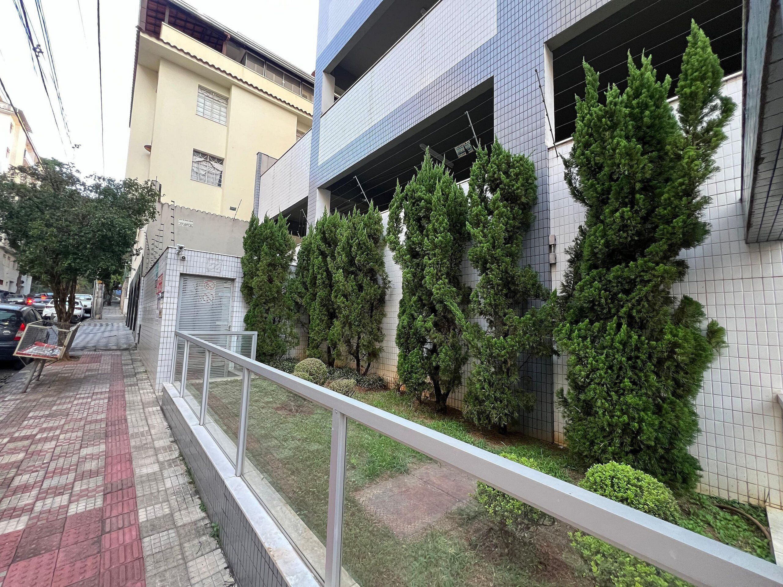 Un edificio con fachada de tejas, un acceso enrejado y un sendero que lleva a una zona arbolada con portones.