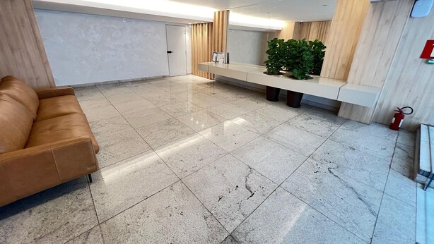 Un vestíbulo amplio con un sofá de cuero, un mostrador de recepción, una planta en maceta y un extintor.