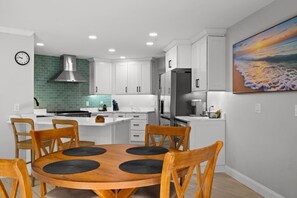 A modern kitchen with white cabinets, a green backsplash, a stainless steel range hood, and a dining area with a round table and wooden chairs. - Sunny Clearwater Oasis W/Private Pool & Back yard (Clearwater)