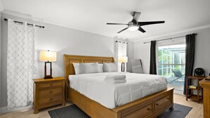Une chambre à coucher avec un lit en bois, deux tables de chevet, un ventilateur de plafond et une vue sur l’extérieur.