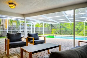 Eine überdachte Terrasse im Freien mit Pool, Sitzgelegenheit und großen Fenstern.