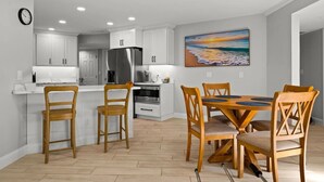 Une cuisine moderne avec des meubles blancs, un réfrigérateur en acier inoxydable et un coin repas comprenant des chaises et une table en bois.
