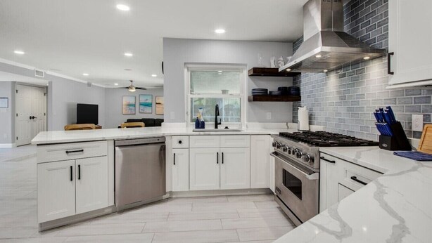 Une cuisine moderne avec des meubles blancs, une cuisinière en acier inoxydable et un dosseret en briques.