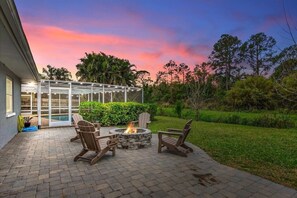 Eine Terrasse mit Feuerstelle, Sitzgelegenheiten im Freien und einer Glasveranda mit Blick auf einen Pool.