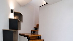 Eine moderne Treppe mit Holzdielen und schwarzen Metallgeländern, die zu einer Zwischenebene mit integrierten Regalen und einer Leuchte führt.