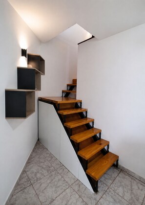 Eine moderne Treppe mit Holzdielen und schwarzen Metallgeländern, die zu einer Zwischenebene mit integrierten Regalen und einer Leuchte führt.