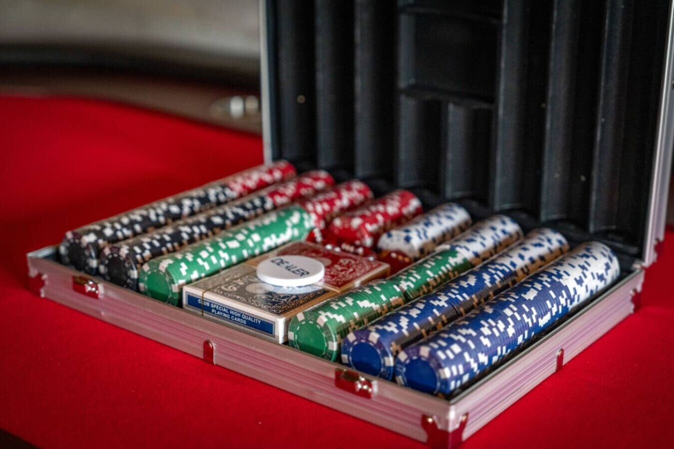 A stack of poker chips in various colors and denominations, a dealer button, and playing cards in a case.