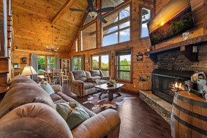A log cabin interior with a fireplace, wooden furniture, and large windows. - Sapphire Sky | Kids Fun Zone | Sauna | Mtn Views (Mineral Bluff)