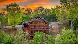 A two-story log cabin with a balcony, surrounded by dense forest. - Sapphire Sky | Kids Fun Zone | Sauna | Mtn Views (Mineral Bluff)