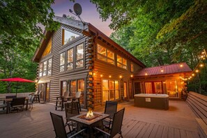 Eine Blockhütte mit einer Terrasse, Sitzgelegenheiten im Freien, einer Feuerstelle und einem Whirlpool.