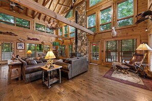 Eine geräumige Hütte mit hohen Decken, großen Fenstern, einem Kamin, Ledermöbeln und einer Wand aus Naturstein.