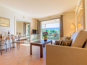 A spacious living room with a large window offering a scenic view, a dining area with a table and chairs, and a cozy seating area with a sofa. - Provence Country Club by Interhome (L'isle sur la Sorgue)
