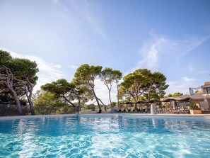 Ein Schwimmbecken mit klarem, blauem Wasser, umgeben von Bäumen und einem Gebäude mit Außenbestuhlung.