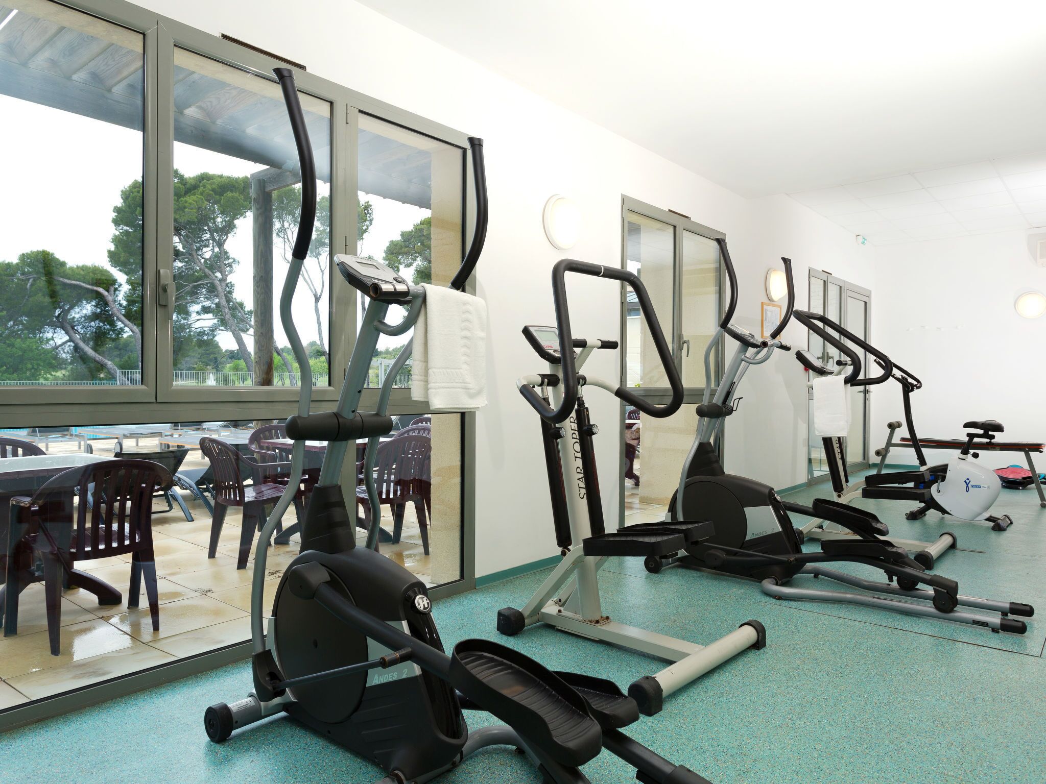 A gym with various exercise equipment, large windows, and a view of outdoor seating.