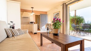 A cozy living area with a sofa, a wooden coffee table, and a dining table set for two. A kitchen is visible in the background, and a balcony with outdoor seating is also seen. - Provence Country Club by Interhome (L'isle sur la Sorgue)